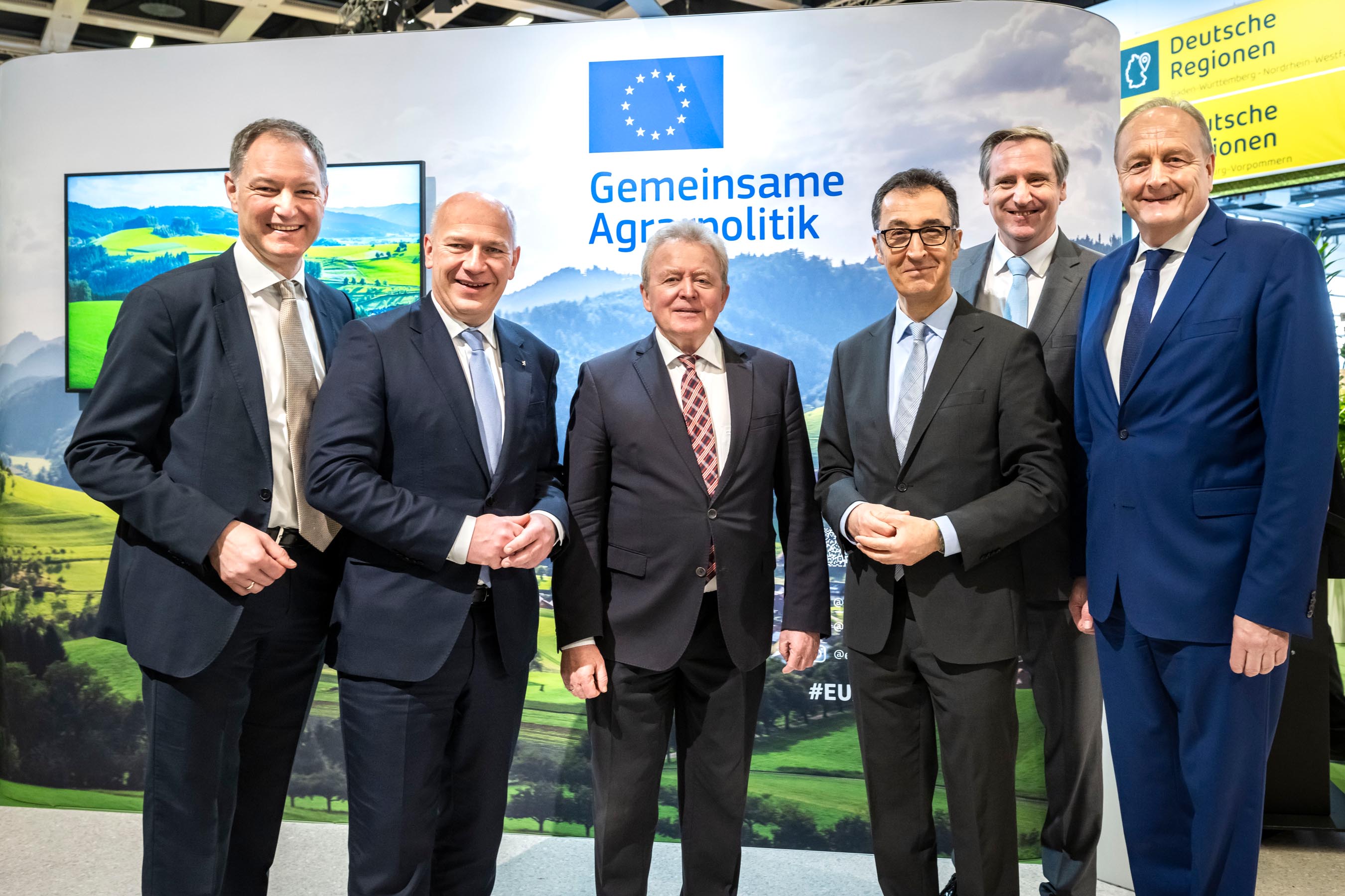 Five men in suits standing in front of a large European flag